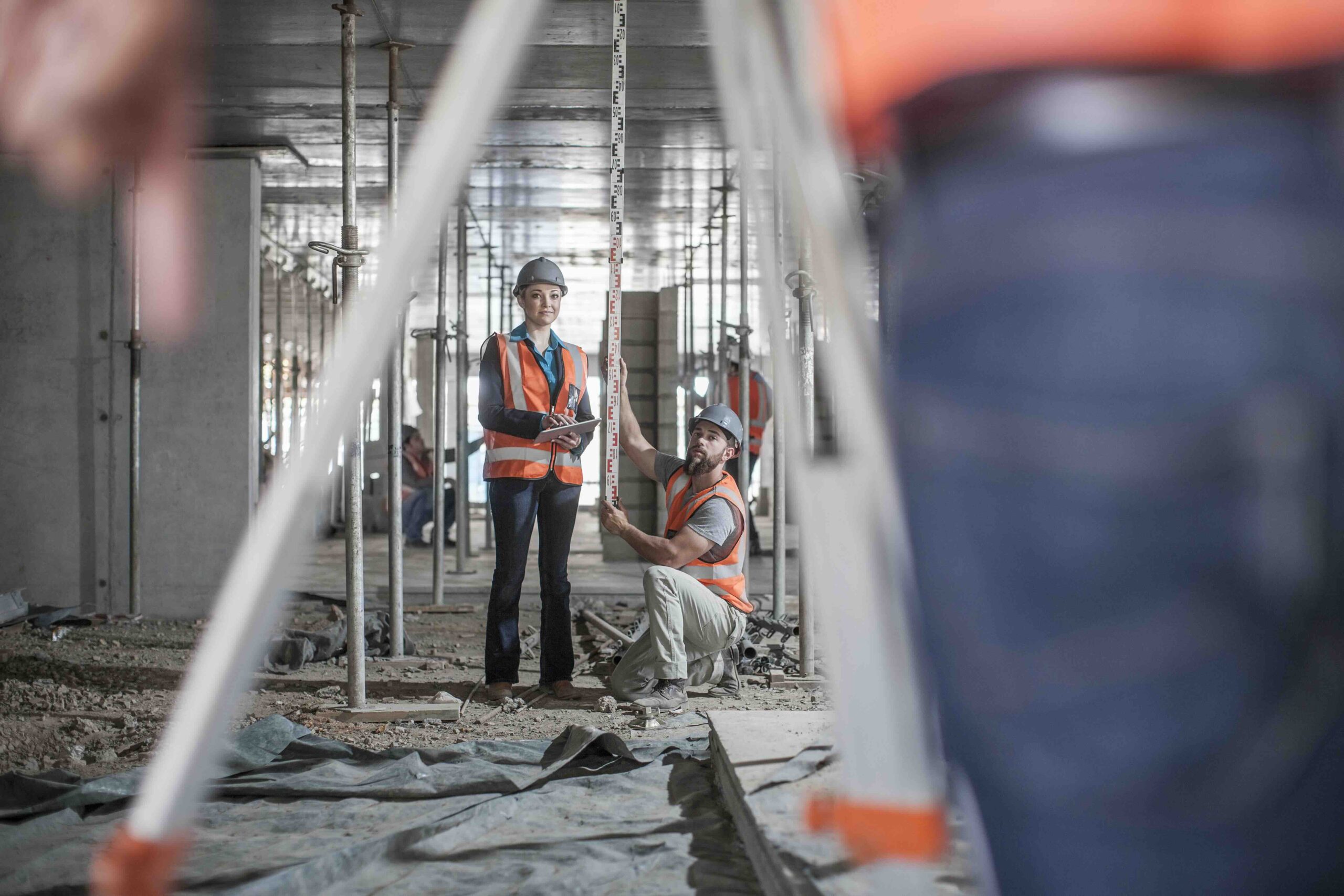 Male and female builders taking measurements for surveyor