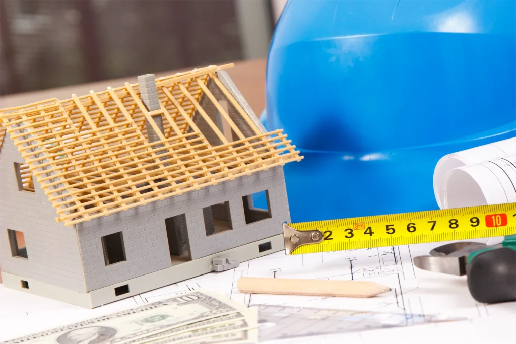House model with tools, blueprints, and hard hat on desk