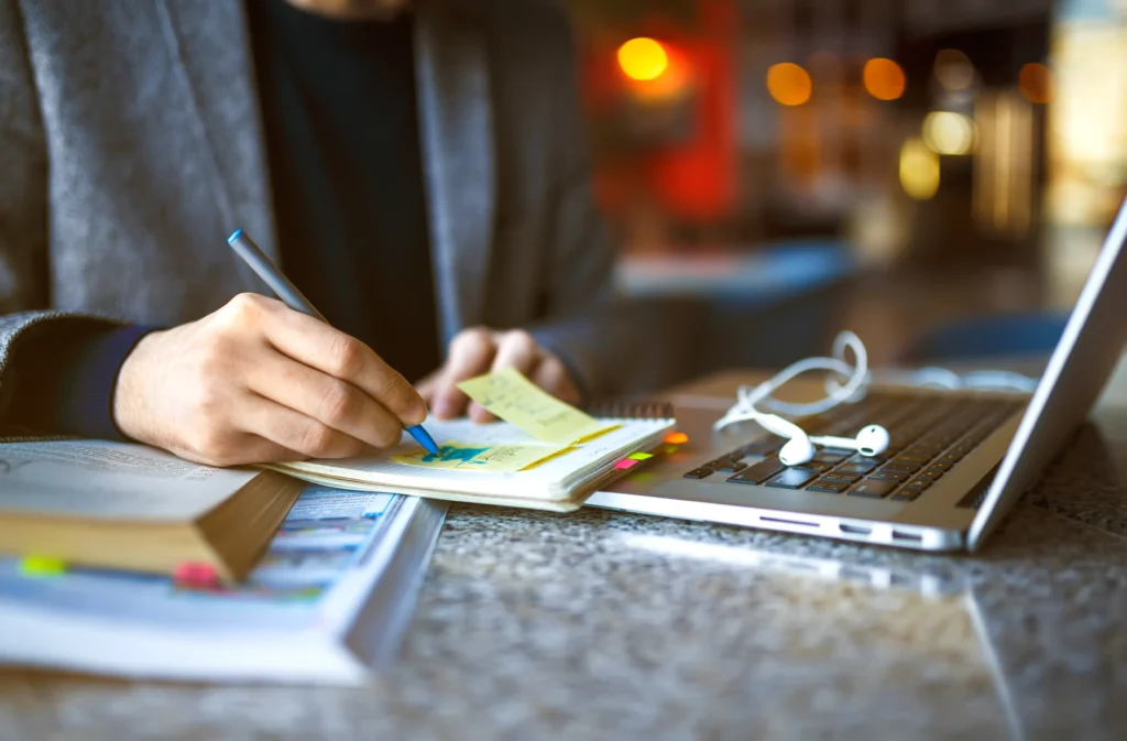Person taking notes with laptop and documents in workspace