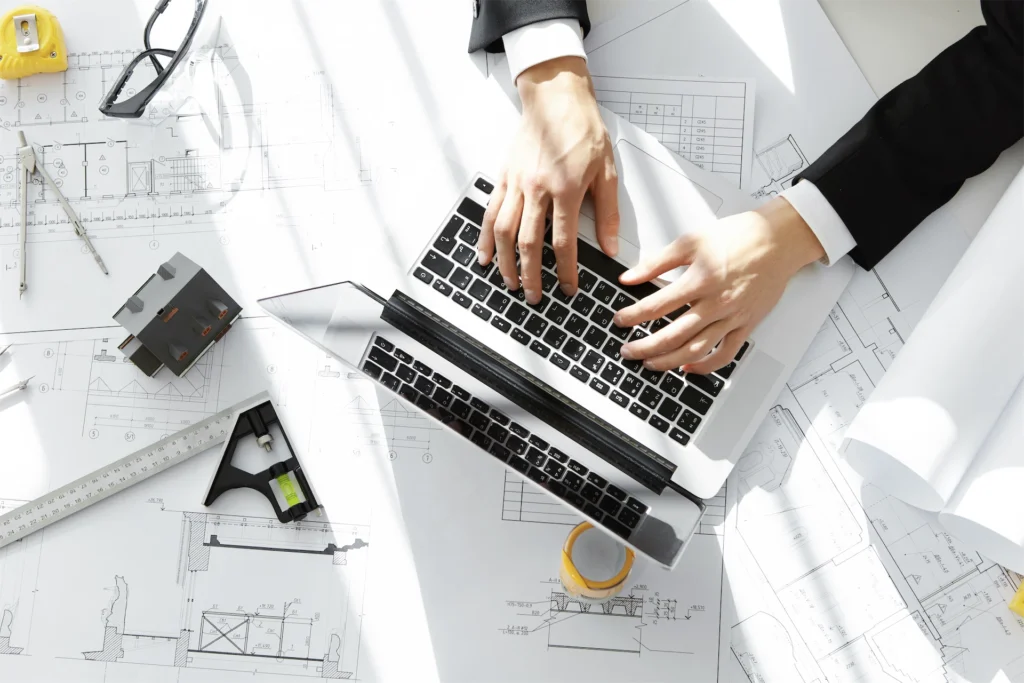 Overhead view of drafting virtual assistant workspace with laptop and plans